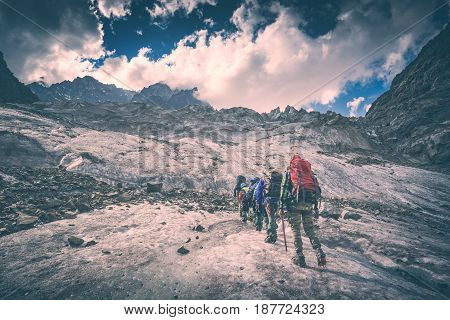 Group of hikers with backpacks climb the glacier to the peak of mountain. Caucasian mountains Georgia Svaneti region. Instagram stylisation.