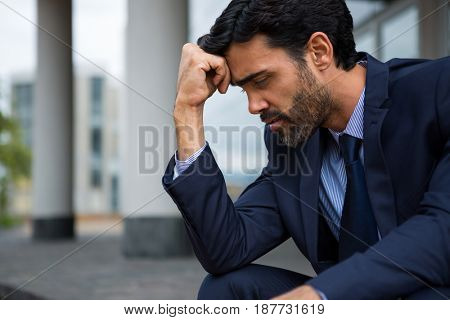 Depressed businessman sitting with hand on forehead in the office premises