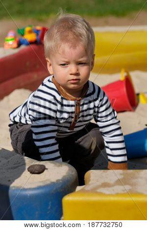 Portrait of toddler child outdoors. One year old baby boy playing with sand at playground sandbox