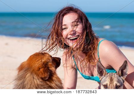 Beautiful girl with two dogs. Happy girl laughing and hugging dogs on the beach. A young woman smiles and hugs two stray dogs.