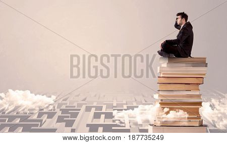 A serious businessman in suit sitting on a pile of giant books in front of a grey wall with clouds, labirynth