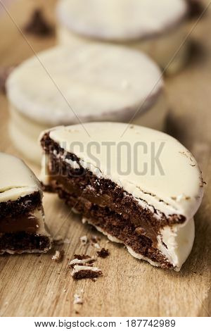closeup of some argentinean-uruguayan alfajores filled with dulce de leche and coated with a white coating on a wooden chopping board, on a rustic table