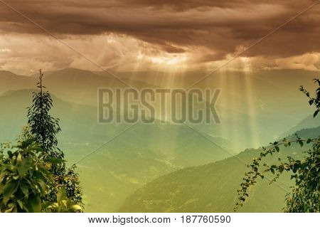 Sun rays coming out of cloud burst - at Rabangla Sikkim India. Trees in foreground and Himalayan mountains in background.