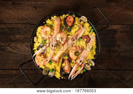 A photo of a Spanish seafood paella in a typical paellera, with mussels, clams, and shrimps, with a place for text, shot from above on a dark rustic texture