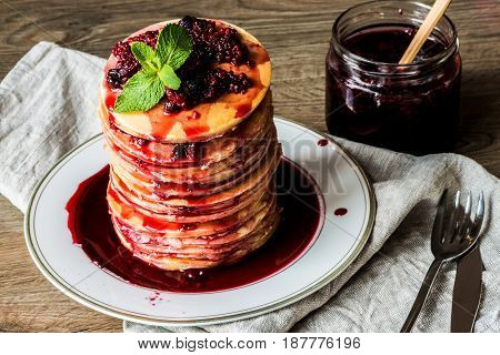 Stack of homemade american pancakes served with jam and strawberries on wooden background.
