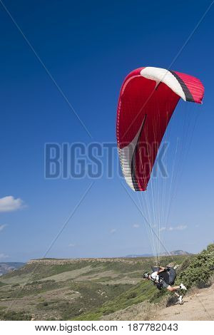 Colorful hang glider in sky over green mountain in Sardinia