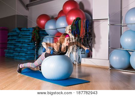 Woman exercising with dumbbells on a fitness ball.