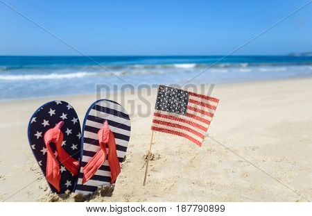 Patriotic USA background with flip flops and American flag on the sandy beach