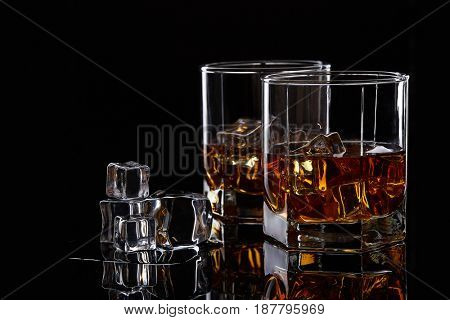 Two glasses of scotch whiskey with ice cubes on a black background.