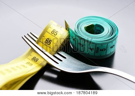 Roll Of Green Measuring Tape Next To Metal Fork