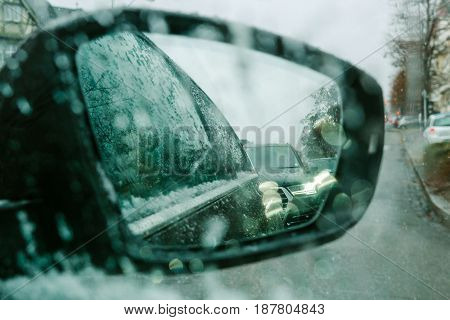 View throu car window at rear view mirror on a snowy day - senn by the driver point ov view personal perspective through wet windshield window