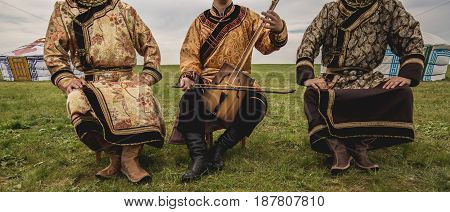 Three Kalmyk musicians in national costumes in the steppe against the background of yurts, the spring steppe. Russia
