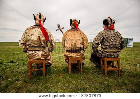 Three Kalmyk musicians in national costumes in the steppe against the background of yurts, the spring steppe. Russia