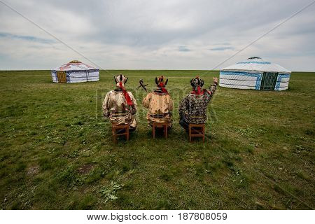 Three Kalmyk musicians in national costumes in the steppe against the background of yurts, the spring steppe. Russia