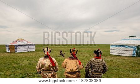Three Kalmyk musicians in national costumes in the steppe against the background of yurts, the spring steppe. Russia