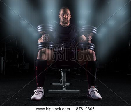 Professional Weightlifter Sits On A Bench With Two Dumbbells On His Lap