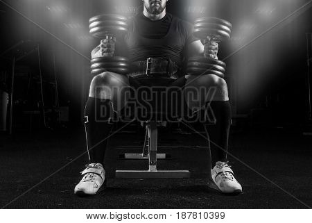 Professional Weightlifter Sits On A Bench With Two Dumbbells On His Lap