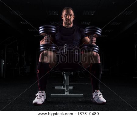 Professional Weightlifter Sits On A Bench With Two Dumbbells On His Lap