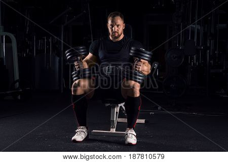 Impressive Athlete Sits On A Bench With Two Dumbbells On His Legs