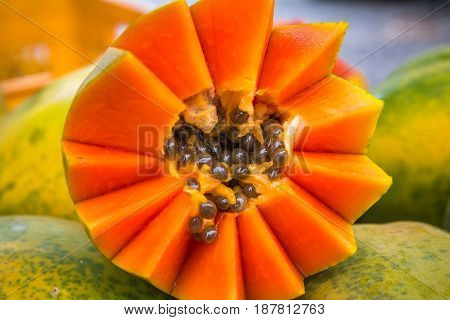 Closeup of bright orange papaya cut artfully with brown seeds surrounded by light green skinned whole papayas in the background