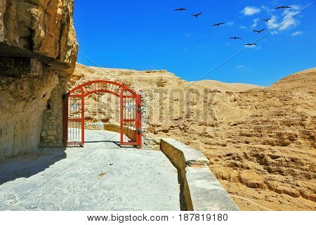 Decorative red gate with a cross on a mountain road going to the temple. Wadi Kelt near Jerusalem