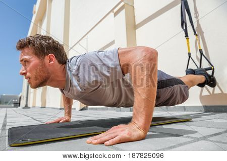 Fitness man doing pushups using suspension straps at fitness centre. Athlete doing bodyweight push-up exercises on floor outdoors.