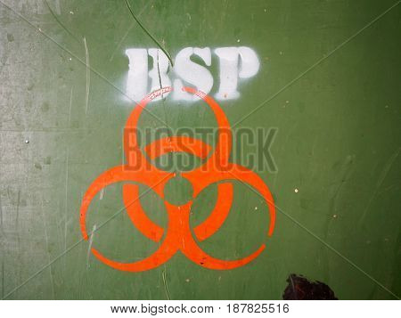 Close-up detail of an orange biohazard symbol painted onto the side of a green medical waste disposal dumpster with many scratch marks on the plastic. Hazardous waste and science concept.