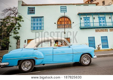 Old blue American car driving urban Cuban capital city