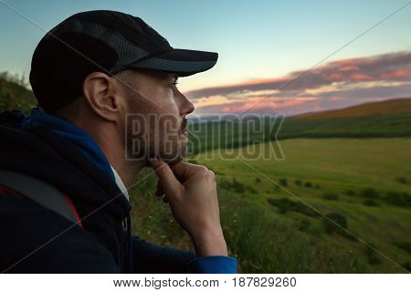 Thoughtful tourist sits on a mountain and looks into the distance to a beautiful sunset.