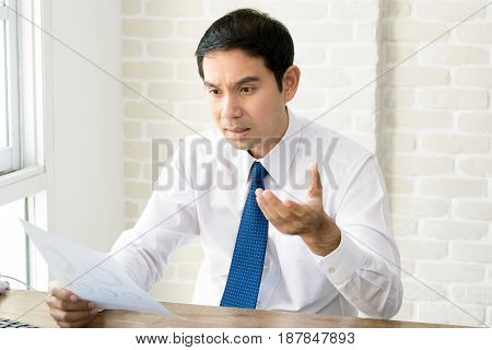 Asian businessman getting upset and disappointed after reading document at his working desk