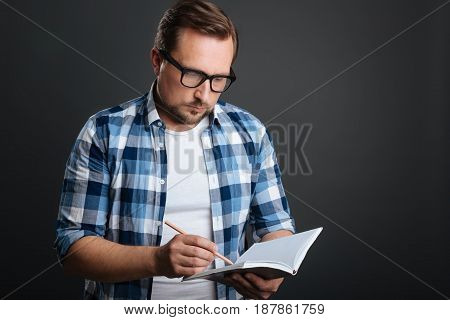 Focused writer. Organized devoted calm guy compiling a schedule while using his journal and a pencil for writing it down
