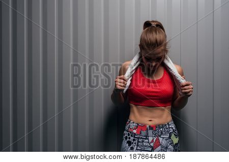 Portrait of young muscular woman wearing sportswear looking down on her abdominal. Fit sporty girl posing against grey wall, copyspace. Fitness motivation concept.