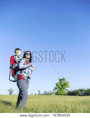 Mother with baby in backpack carrier is hiking in mountains. Tourist is carrying a child on his back on the nature.