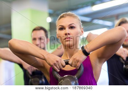 sport, fitness, weightlifting and people concept - woman with kettlebell and heart-rate tracker at group training exercising in gym