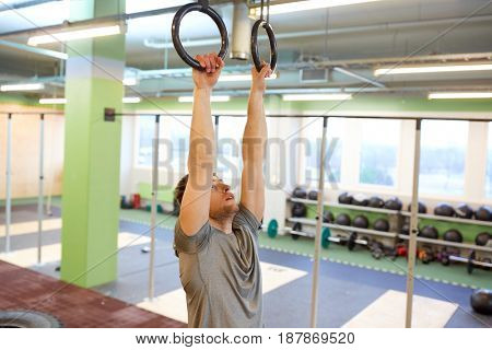 sport, fitness, training and people concept - man exercising and doing ring pull-ups in gym