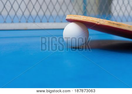 pingpong rackets and ball and net on a blue pingpong table close up