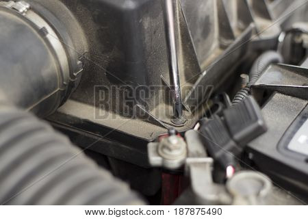 Unscrew the screw from the air filter cover with a screwdriver. The mechanic in the protective gloves unscrew the screw with the screwdriver from the air filter cover.