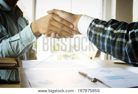 Close-up of two business people shaking hands while sitting at the working place.