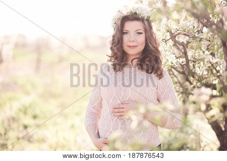 Smiling pregnant girl 25-29 year old holding tummy outdoors. Looking at camera. Summer time. Maternity. 20s.