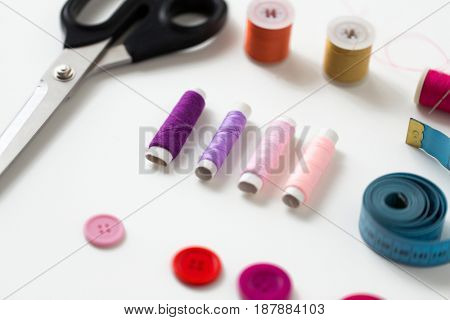 needlework and tailoring concept - scissors, sewing buttons, spools of thread and tape measure