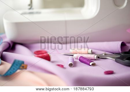 needlework, technology and tailoring concept - sewing machine with scissors, spools of thread, buttons and fabric