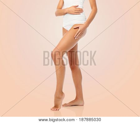 beauty, people and bodycare concept - legs of beautiful young woman in white underwear over beige background