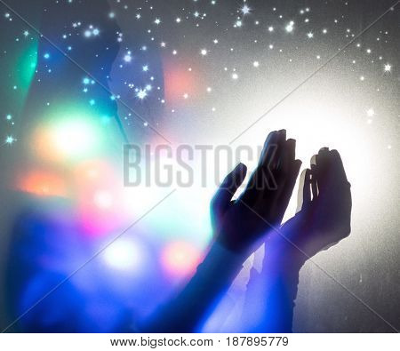 Hands praying in dark room with nice lights around her