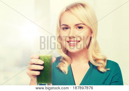 healthy eating, vegetarian food, diet, detox and people concept - smiling young woman drinking green vegetable juice or smoothie from glass at home