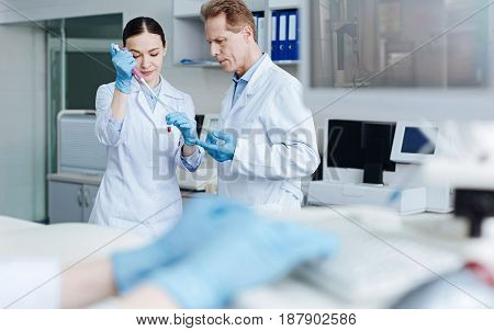 Checkup of genetic code. Delighted female bowing head, holding medical dropper while taking exemplar