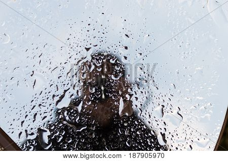 Unrecognizable man silhouette reflection on a wet window. Photographer taking selfie on a mirror.