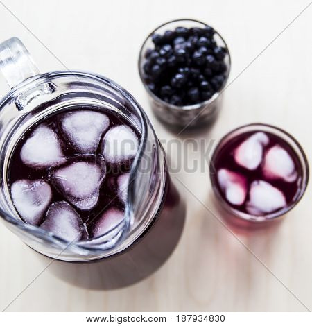 Blueberry juice in a decanter and a glass next to frozen berries