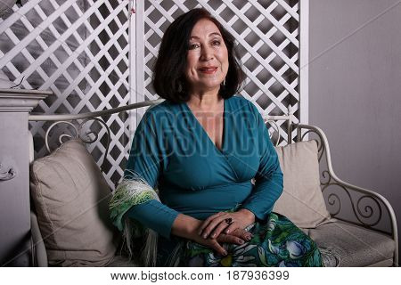 Mature Asian woman sitting on a couch in a luxurious dress.