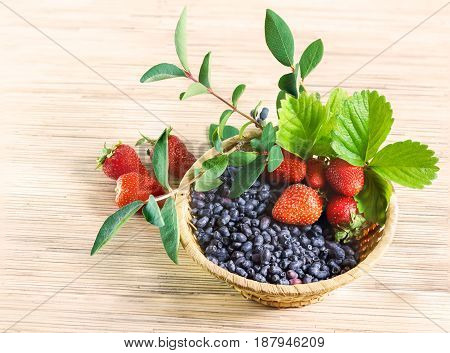Berries red ripe strawberry and blue honeysuckle far East in a wicker basket with leaves on the table