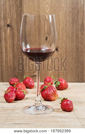 Glass with red wine on a wooden table with scattered ripe strawberries